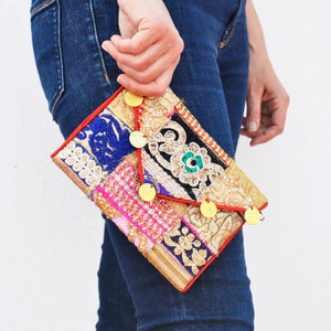 Może przedstawiać: Kolorowa patchworkowa kopertówka z złotymi akcentami i czerwoną lamówką. Torebka wykonana jest z różnych tkanin i ma unikalny, bohemiczny styl.