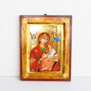 May include: A framed religious icon depicting the Virgin Mary holding baby Jesus. The icon is painted in a traditional style with gold accents and features two angels on either side of the central figures. The icon is framed in a dark wood frame.
