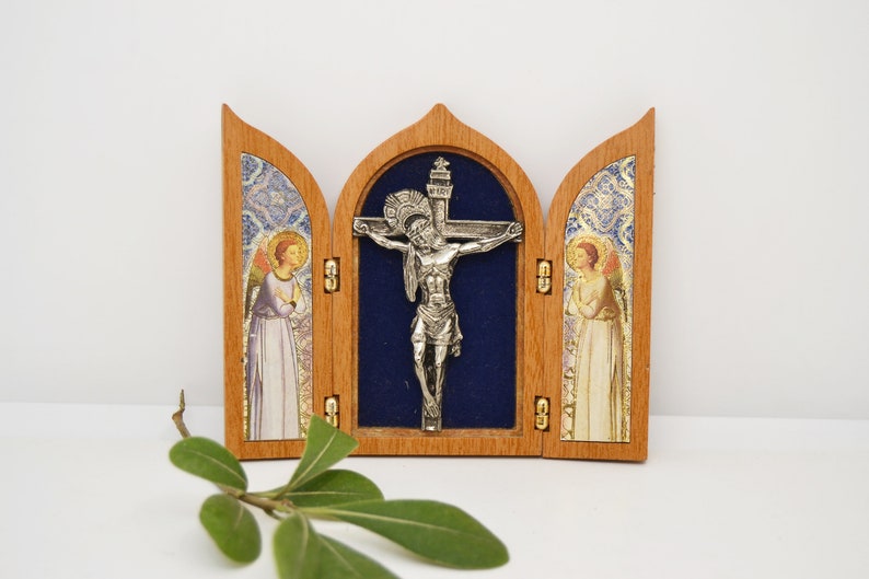 May include: A wooden triptych with a silver crucifix in the center panel. The side panels feature images of angels with gold accents. The triptych is closed and has a blue velvet interior.