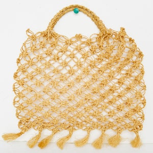 May include: A beige crocheted tote bag with fringe detailing. The bag has a knotted design and a turquoise bead on the handle.
