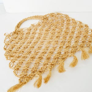 May include: A beige crocheted tote bag with fringe detailing. The bag is made of a natural fiber and has a woven texture.