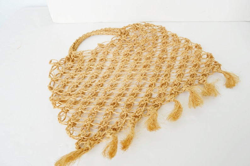 May include: A beige crocheted tote bag with fringe detailing. The bag is made of a natural fiber and has a woven texture.