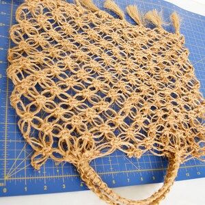 May include: A tan crocheted tote bag with long fringe tassels. The bag is made of natural fibers and has a woven texture.