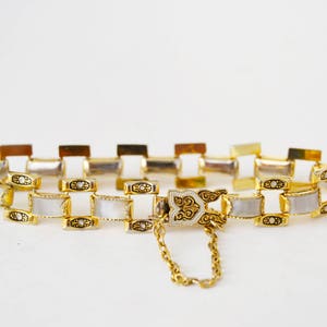 May include: A gold-tone bracelet with a white enamel design. The bracelet has a decorative clasp and a chain.