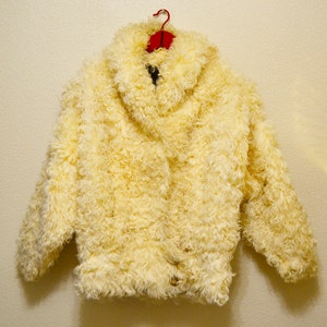 Puede incluir: Una chaqueta de piel sintética de color crema con cuello alto y cierre de botones.