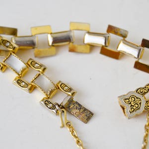May include: A gold tone bracelet with a chain link design and white enamel accents. The bracelet has a decorative clasp with a floral design.