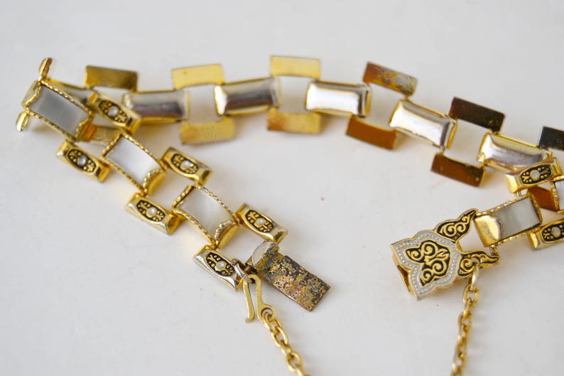 May include: A gold tone bracelet with a chain link design and white enamel accents. The bracelet has a decorative clasp with a floral design.