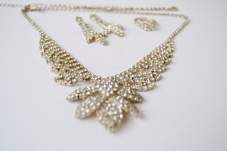 Pu&ograve; includere: Un set di collana e orecchini in tinta oro con strass trasparenti. La collana presenta una catena delicata con un ciondolo a forma di foglia.