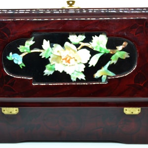 Peut inclure: Une bo&icirc;te &agrave; bijoux rectangulaire en bois laqu&eacute;, de couleur bordeaux fonc&eacute;. La bo&icirc;te pr&eacute;sente un panneau d&eacute;coratif central avec un motif floral en nacre et un fermoir en laiton.