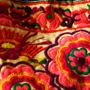 May include: Close-up of colorful embroidered fabric with a floral pattern. The fabric is cream-colored with red, pink, yellow, green, and purple embroidery.