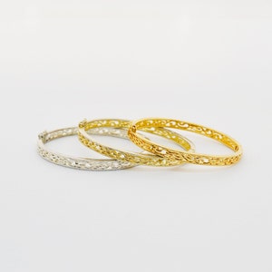 Può includere: Tre braccialetti rigidi in filigrana oro e argento. I braccialetti sono impilati uno sopra l'altro.