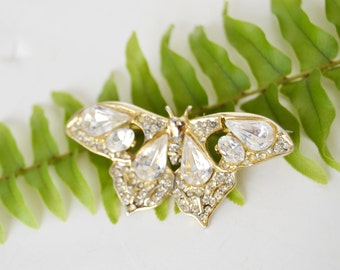 Puede incluir: Un broche de mariposa dorada con detalles de pedrería transparente.