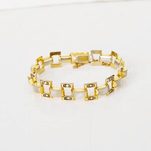 May include: A gold-tone bracelet with white rectangular links. The links are set with small, clear stones.