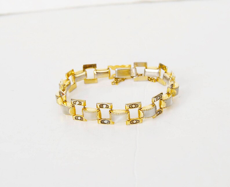 May include: A gold-tone bracelet with white rectangular links. The links are set with small, clear stones.