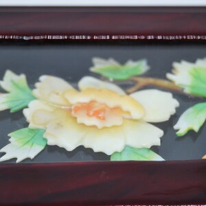 Peut inclure: Gros plan sur un cadre en bois d&eacute;coratif avec un motif floral. Le cadre est de couleur brun rouge&acirc;tre fonc&eacute;, et le motif floral pr&eacute;sente une fleur cr&egrave;me avec un centre orange, des feuilles vertes et une tige brune.