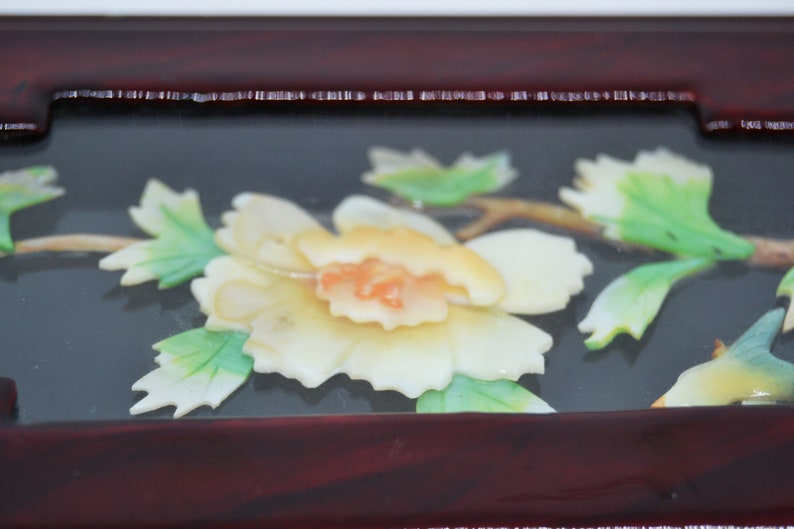 Peut inclure: Gros plan sur un cadre en bois d&eacute;coratif avec un motif floral. Le cadre est de couleur brun rouge&acirc;tre fonc&eacute;, et le motif floral pr&eacute;sente une fleur cr&egrave;me avec un centre orange, des feuilles vertes et une tige brune.