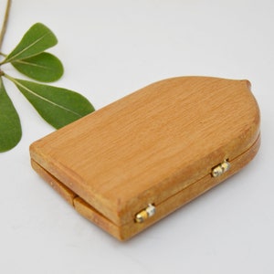 May include: A small, wooden box with a hinged lid. The box is closed and has a light brown color. The box has a rounded top and a slightly pointed bottom.
