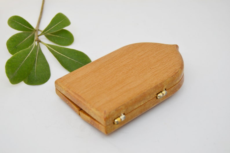 May include: A small, wooden box with a hinged lid. The box is closed and has a light brown color. The box has a rounded top and a slightly pointed bottom.