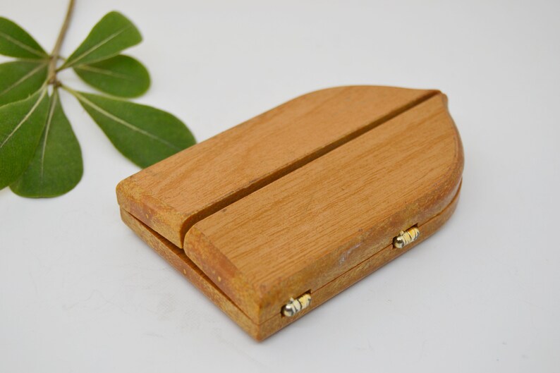 May include: A small wooden box with a hinged lid and a decorative arch shape. The box is made of light brown wood and has two small gold hinges.