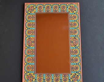 May include: A decorative mirror with a colourful, ornate frame. The frame features a repeating pattern of blue, yellow and orange geometric shapes.