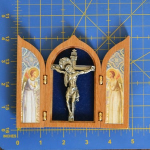 May include: A small wooden triptych with a silver crucifix in the center panel. The side panels feature images of angels with gold accents. The triptych is approximately 4 inches wide.