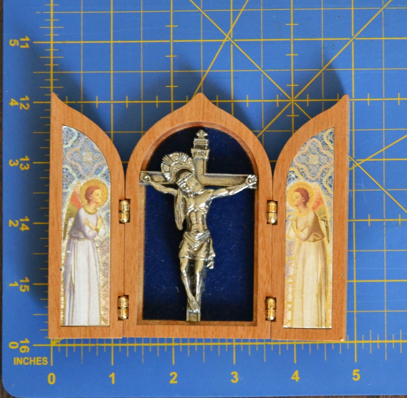 May include: A small wooden triptych with a silver crucifix in the center panel. The side panels feature images of angels with gold accents. The triptych is approximately 4 inches wide.