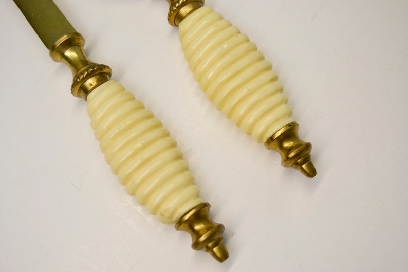 May include: A pair of brass letter openers with ivory-colored handles. The handles have a spiral design.