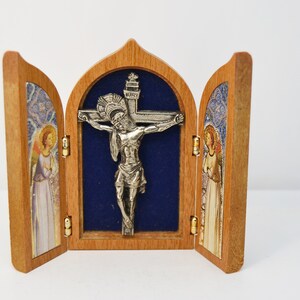 May include: A wooden triptych with a silver crucifix in the center panel. The side panels feature images of angels with stained glass backgrounds.