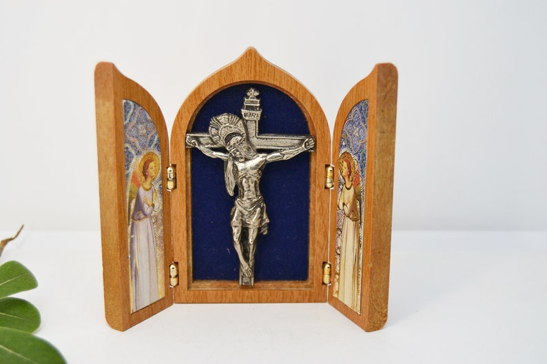 May include: A wooden triptych with a silver crucifix in the center panel. The side panels feature images of angels with stained glass backgrounds.