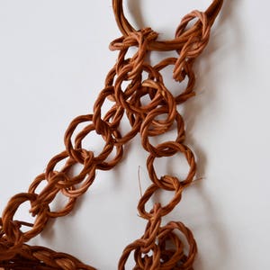 May include: A brown woven chain made of natural fibers, with a looped end. The chain is made of multiple interconnected rings.