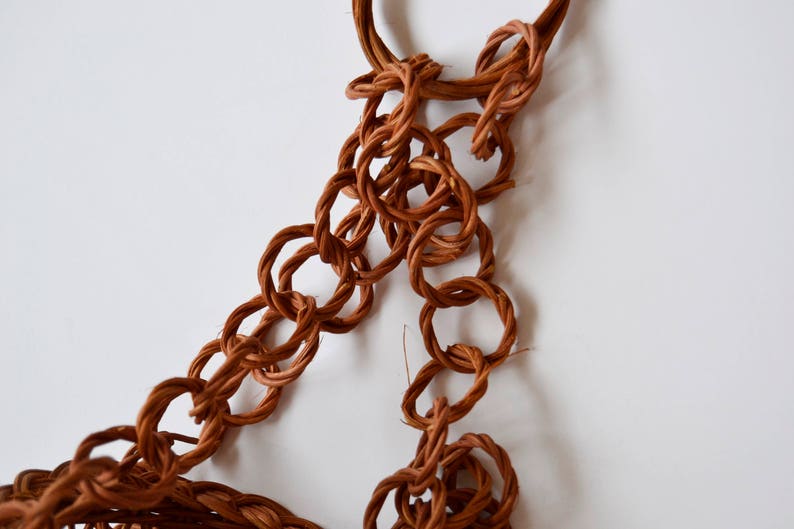 May include: A brown woven chain made of natural fibers, with a looped end. The chain is made of multiple interconnected rings.