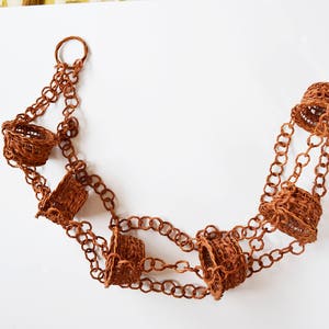 May include: A brown chain with six small brown woven baskets hanging from it. The chain is looped at the top and the baskets are evenly spaced along the chain.