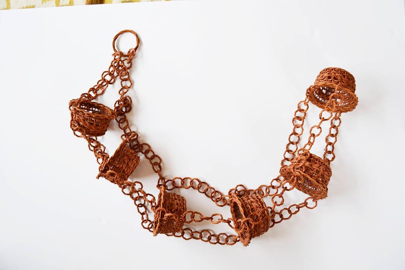 May include: A brown chain with six small brown woven baskets hanging from it. The chain is looped at the top and the baskets are evenly spaced along the chain.