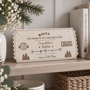 May include: A rectangular wooden plaque shaped like a ticket with scalloped edges, featuring laser-engraved text that reads: YOU MADE IT ON THE NICE LIST, Congratulations SOFIA, You are officially on my nice list, and Signed by: Santa Claus.