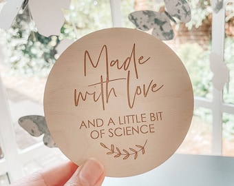 May include: A round wooden sign with the text "Made with love and a little bit of science" in a brown font. The sign has a small leafy design at the bottom.
