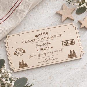 May include: A rectangular wooden ticket with scalloped edges featuring laser-engraved text that reads YOU MADE IT ON THE NICE LIST, Congratulations SOFIA, You are officially on my nice list, and Signed by: Santa Claus, with pine tree graphics.