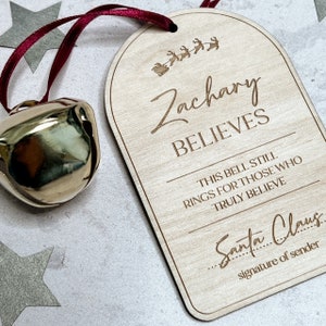 May include: A wooden Christmas bell tag with the text "Zachary Believes" and "This bell still rings for those who truly believe". There is a line for a signature and the text "Santa Claus".