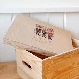 May include: A wooden Christmas Eve box with a hinged lid. The lid features a colorful illustration of three nutcracker figures and the text "Thomas' Christmas Eve Box".