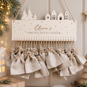 May include: A wooden wall-hanging Christmas advent calendar featuring a laser-cut design of pine trees and houses. The board is engraved with the text Oliver's CHRISTMAS ADVENT CALENDAR and numbers 1 through 25, with 25 small beige burlap bags.