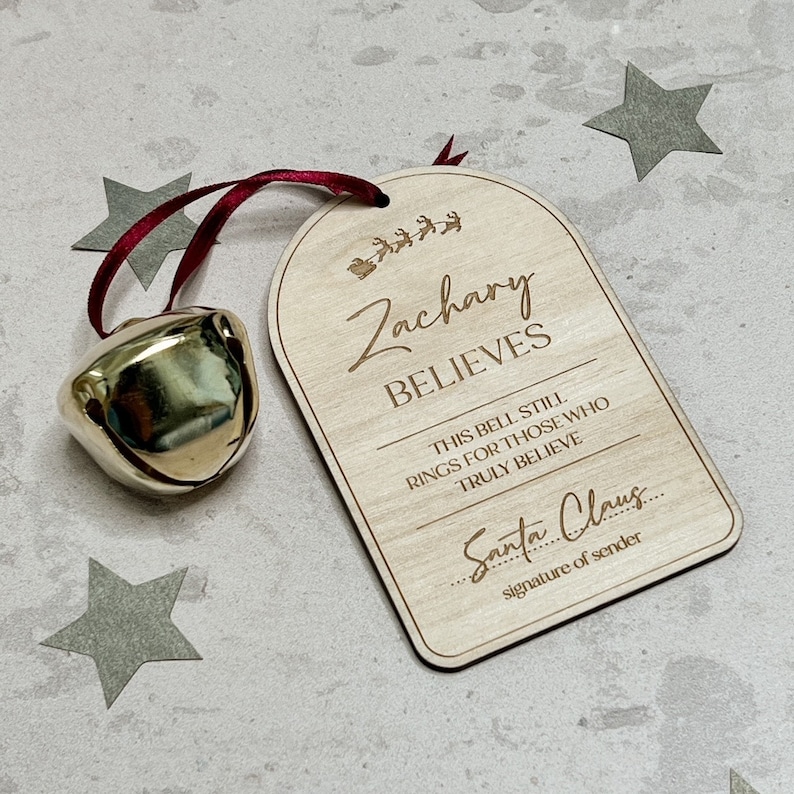 May include: A wooden Christmas bell ornament with the text "Zachary Believes" and "This bell still rings for those who truly believe". There is a line for a signature that says "Santa Claus" and "signature of sender".