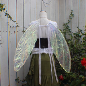May include: A pair of iridescent fairy wings with a white and green dress and a brown belt.