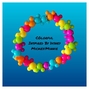 May include: A colorful circle of Mickey Mouse and Minnie Mouse head-shaped charms. The charms are in various colors, including red, orange, yellow, green, blue, and purple. The text "COLORFUL INSPIRED BY DISNEY MICKEY/MINNIE" is written in black in the center of the circle.