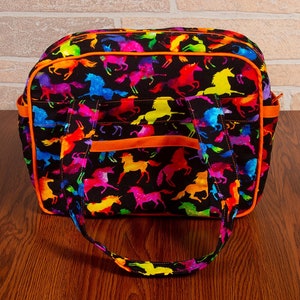 Pode incluir: Uma bolsa tote preta com estampa de unicórnio colorida e acabamento laranja. A bolsa tem um fecho de correr superior e duas alças.