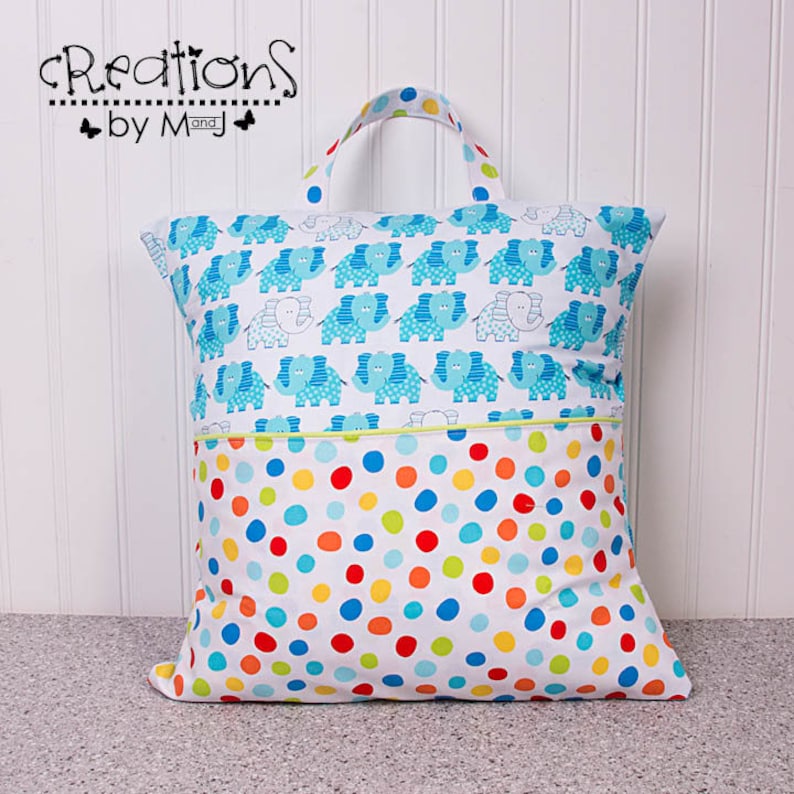 Pode incluir: Uma bolsa de armazenamento de tecido branco com uma estampa de elefantes azul e branco de um lado e um fundo branco com bolinhas coloridas do outro lado. A bolsa tem uma al&ccedil;a e um bolso com z&iacute;per.