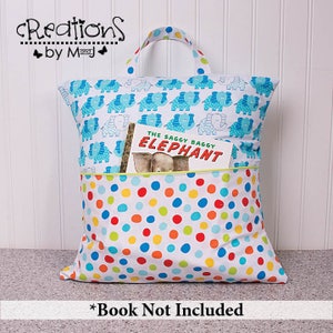 Pode incluir: Uma bolsa de livro branca com uma estampa de elefantes azuis de um lado e uma estampa de bolinhas coloridas do outro. A bolsa tem uma al&ccedil;a e um bolso na frente. O texto "The Saggy Baggy Elephant" &eacute; vis&iacute;vel no livro dentro da bolsa. O texto "Book Not Included" est&aacute; na parte inferior da imagem.