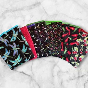 May include: A collection of seven fabric items with various patterns. Designs include dragonflies, scissors, musical notes, chili peppers, and cherries. Each item has a different colored border, such as blue, red, and green.
