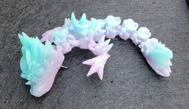 Pu&ograve; includere: Una scultura in resina di un drago di colore blu pastello e viola con dettagli floreali. Il drago &egrave; arrotolato su se stesso con la testa appoggiata sulla coda.