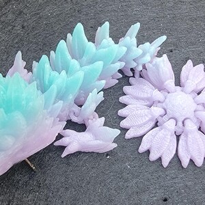 Pu&ograve; includere: Un paio di sculture decorative in cristallo color pastello. Una scultura &egrave; una figura di drago con un gradiente dal rosa al blu. L'altra scultura &egrave; una forma di fiore di colore viola.