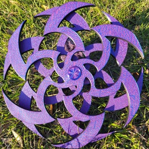 May include: A purple and blue iridescent wooden starburst with a central metal disc. The starburst is made of multiple layers of wood, each with a different pattern.