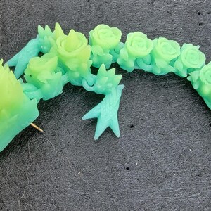 Pu&ograve; includere: Uno spillo in resina verde e blu a forma di drago con un design floreale. Il drago &egrave; arrotolato su se stesso con la testa rivolta a sinistra. Lo spillo &egrave; attaccato a un retro di spillo dorato.